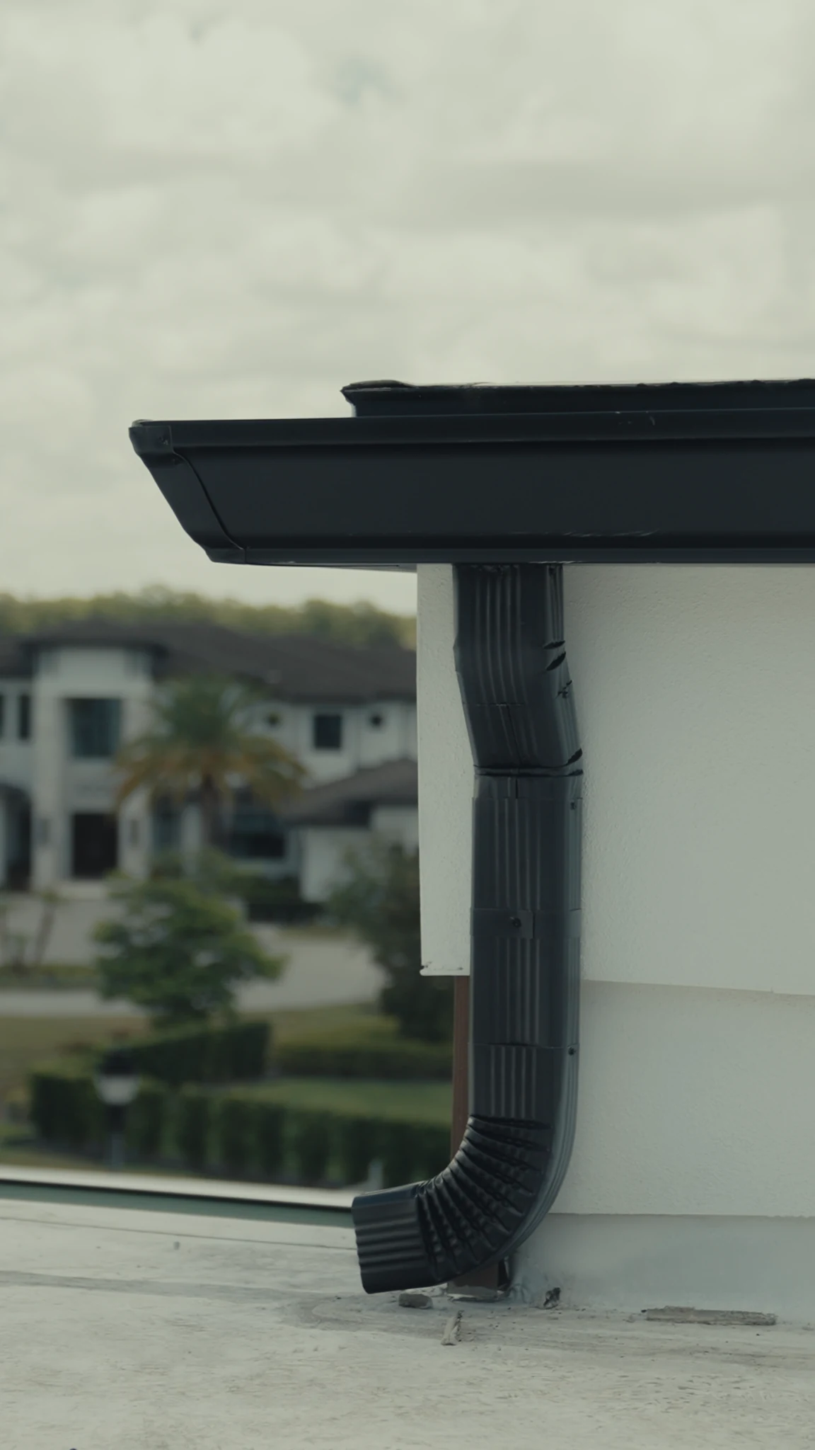 Black downspout secured against a white exterior wall with the roofline visible above