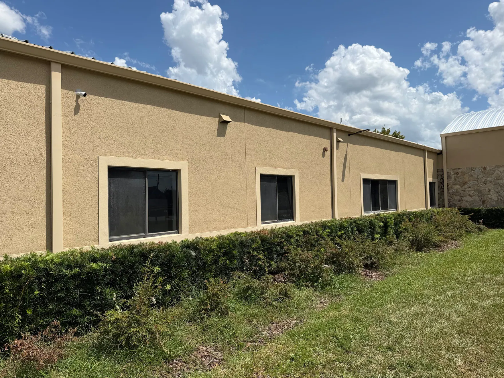 Long roof-edge gutter line on a tan commercial building above windows and landscaping