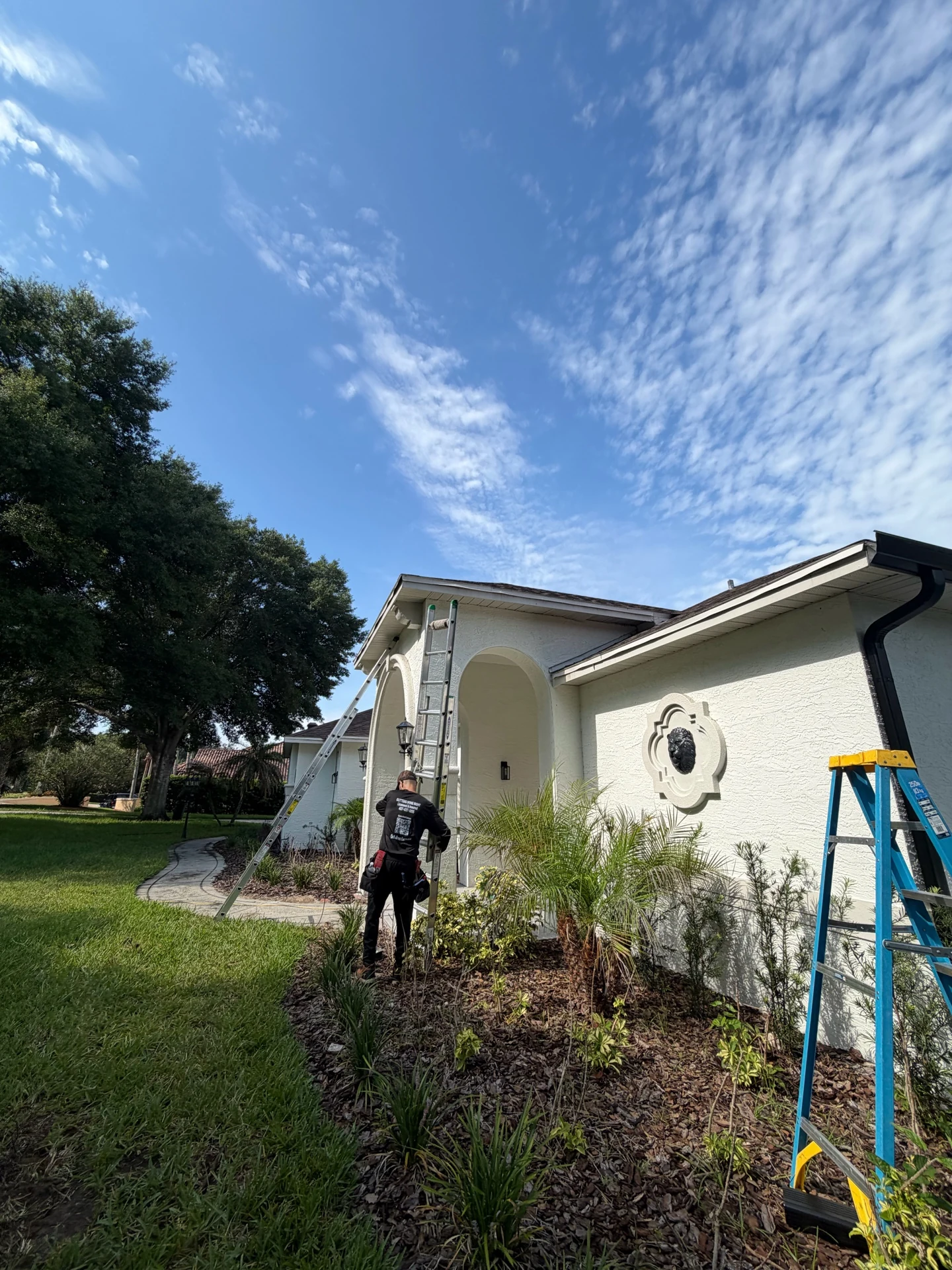 Installer beside a ladder at a white home with black gutters and vertical downspouts