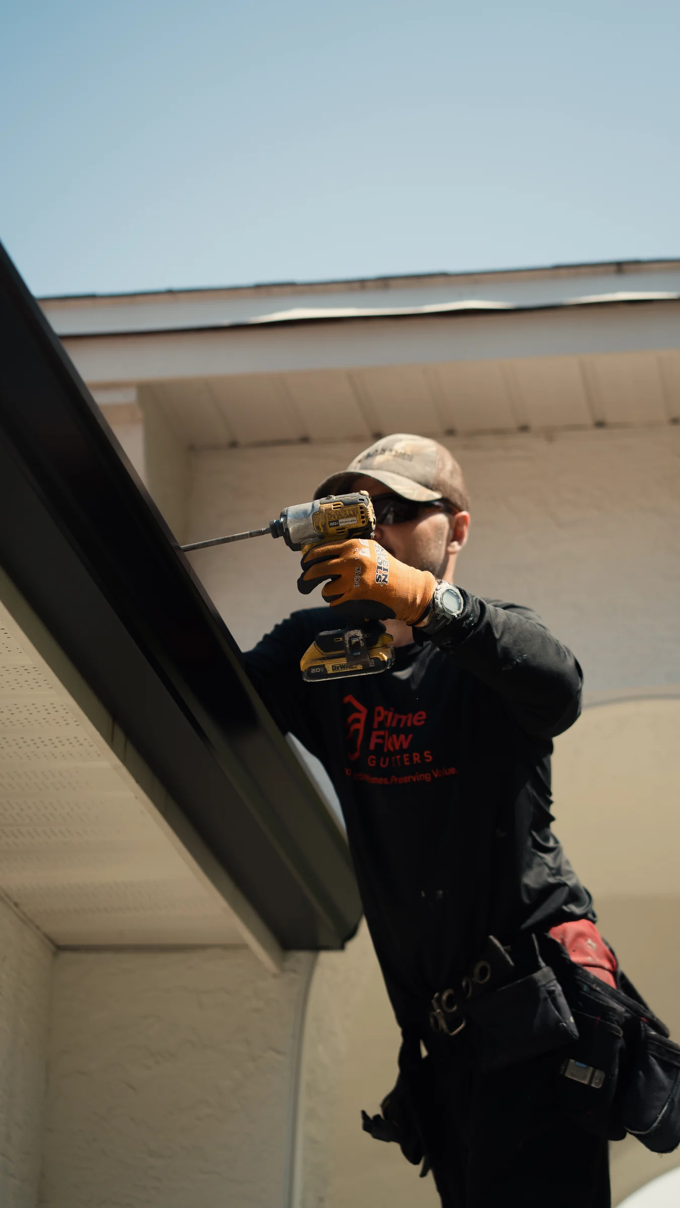 PrimeFlow field team member fastening a dark gutter system along a residential roof edge