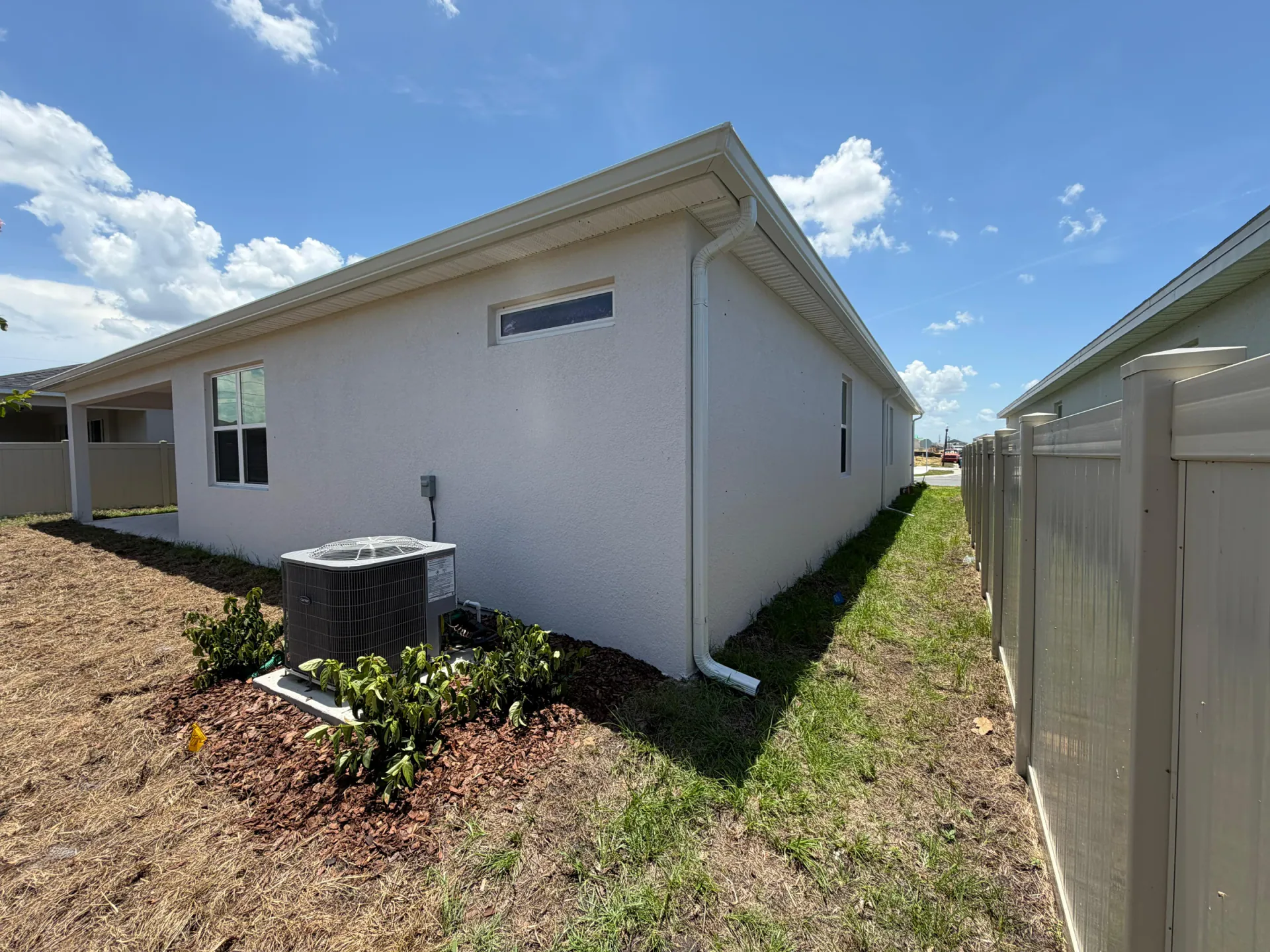 White downspout routed beside an outdoor air-conditioning unit on a residential side wall