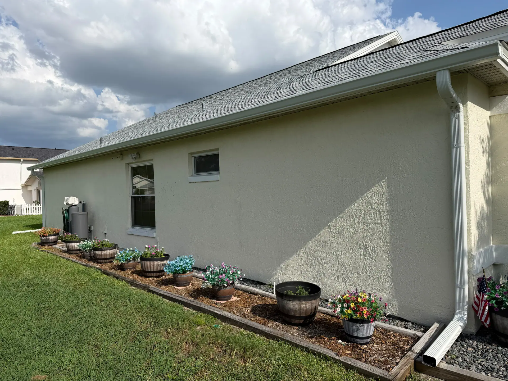 White seamless gutter and downspout along a light stucco side wall with planters below